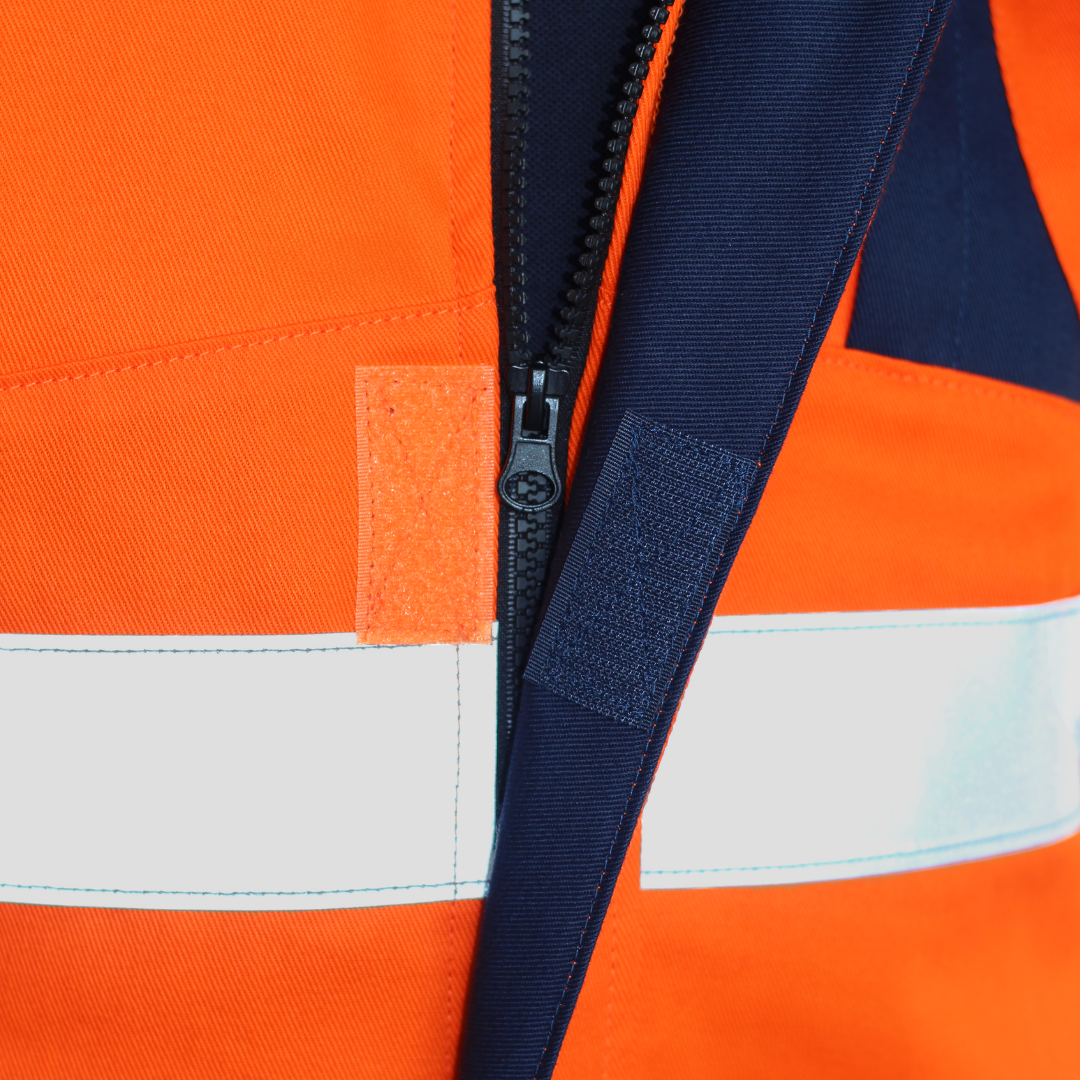 Detalle de cierre frontal de geólogo ignífugo FIREWEAR® naranjo y azul para hombre.