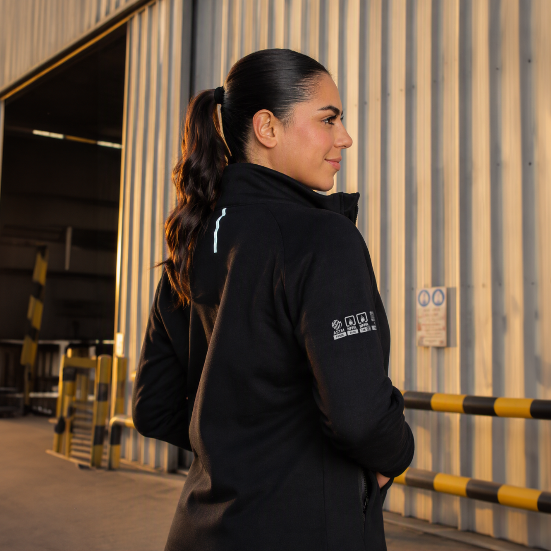 Mujer usando polerón ignífugo FIREWEAR® negro en entorno industrial.