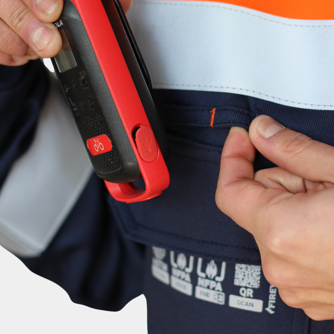 Detalle de bolsillo para radio de chaqueta ignífuga FIREWEAR® bicolor azul y naranjo para hombre.