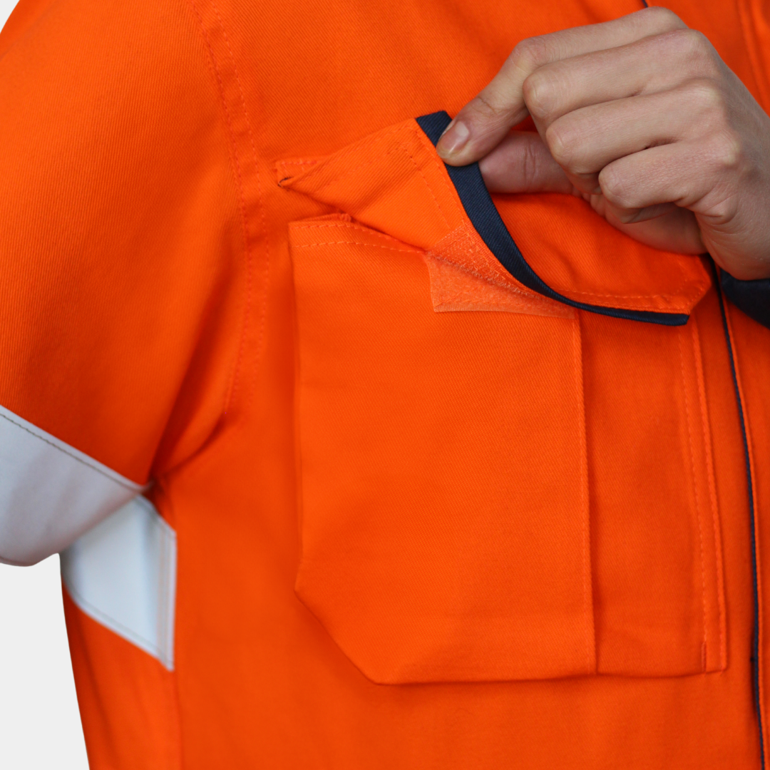 Detalle de bolsillo de pecho de chaqueta ignífuga FIREWEAR® bicolor naranjo y azul para hombre.