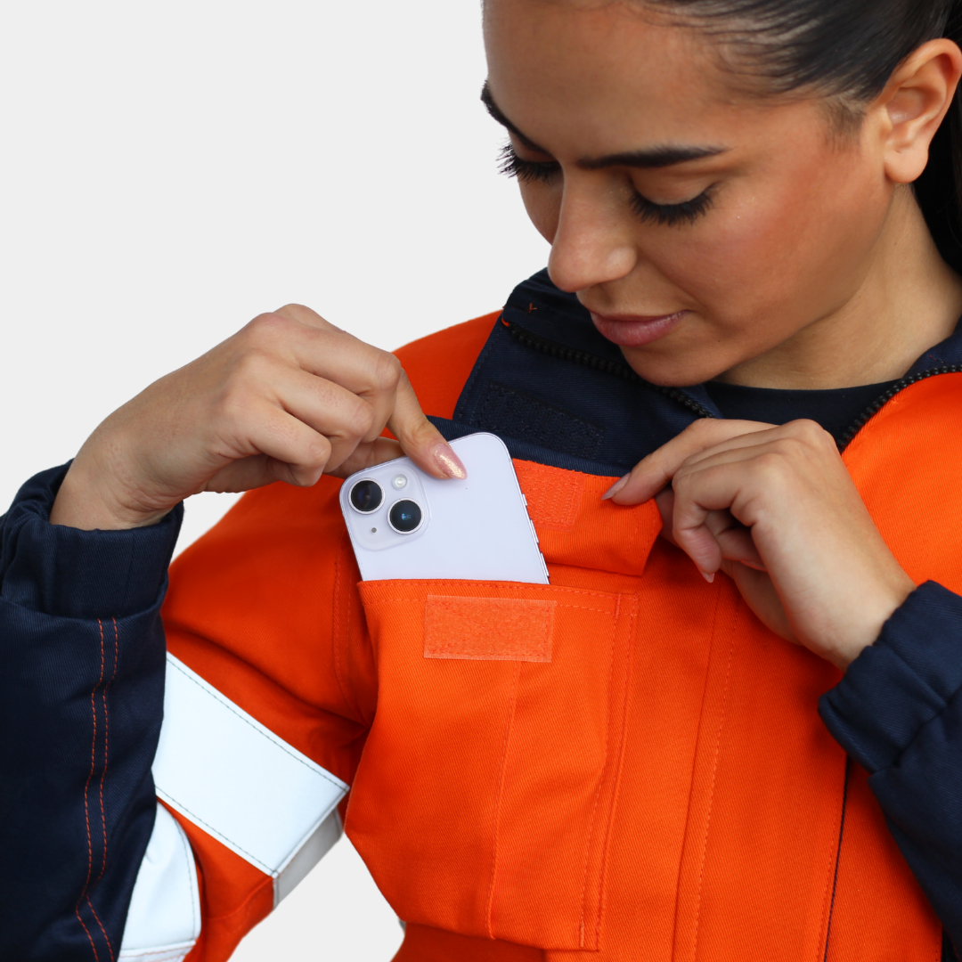 Detalle de bolsillo de pecho de chaqueta ignífuga FIREWEAR® bicolor naranjo y azul para mujer.