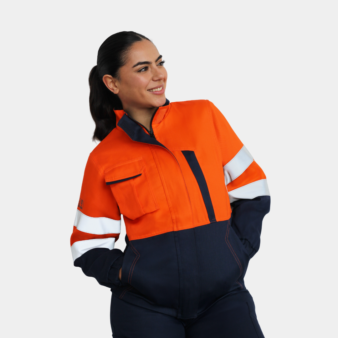 Mujer usando chaqueta ignífuga FIREWEAR® bicolor naranjo y azul con brazos cruzados.