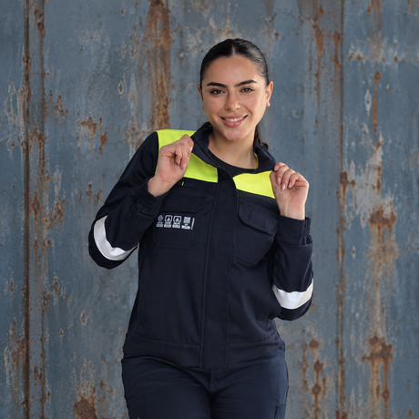 Mujer usando chaqueta ignífuga FIREWEAR® azul marino con detalles de alta visibilidad y cintas reflectantes.