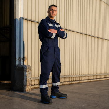 Hombre usando overol ignífugo FIREWEAR® azul marino en vista frontal durante trabajo industrial.
