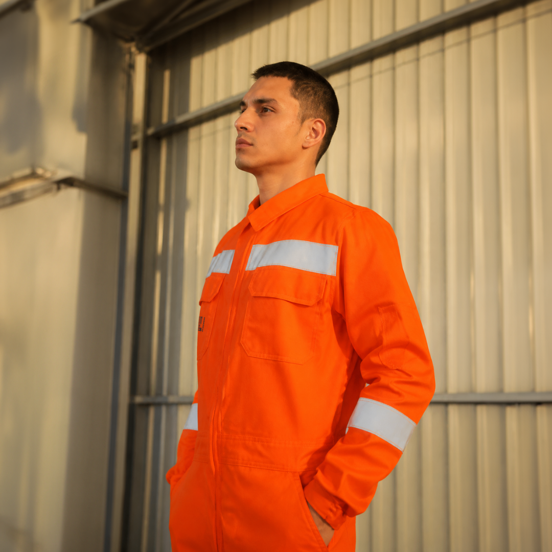 Hombre usando overol ignífugo FIREWEAR® naranjo en vista lateral en entorno industrial.